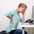 a woman sitting at a desk and has pain in the back. symbol photo
